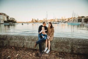 Baby photography - A family cuddle their baby girl as they sit beside the water