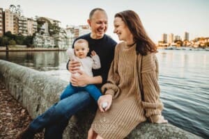 Baby photography - parents cuddle their baby girl as they sit beside the water