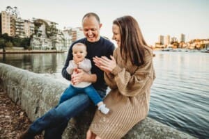 Baby photography - parents cuddle their baby girl as they sit beside the water