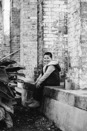 Sydney Family Photographer: a little boy sits against a rustic brick wall