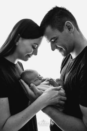 Newborn Photography: a baby boy sleeps in the arms of his parents