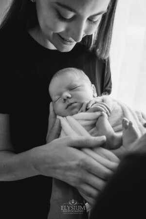 Newborn Photography: a baby boy sleeps in the arms of his mum