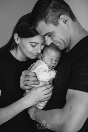 Newborn Photography: a baby boy sleeps in the arms of his parents