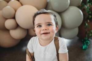 Cake Smash Photographer: a smiley baby boy sits against a balloon wall