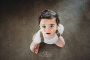 Cake Smash Photographer: a baby boy sits on the floor looking up