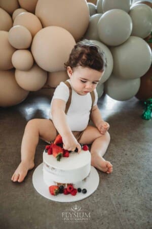 Cake Smash Photographer: a baby boy sits covered in icing pulling faces