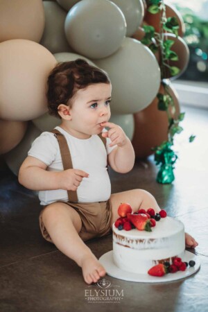 Cake Smash Photographer: a baby boy touches the icing and berries on his cake