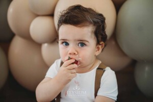 Cake Smash Photographer: a baby boy sits eating a berry and icing