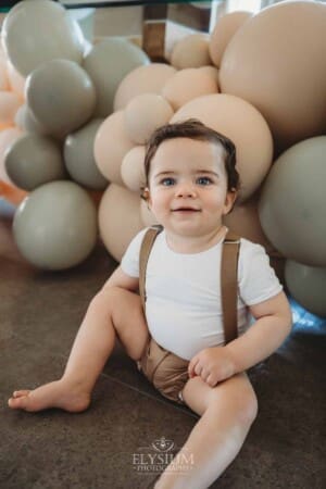 Cake Smash Photographer: a baby boy sits against a balloon wall