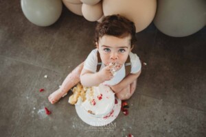 Cake Smash Photographer: a baby boy puts a fistful of cake in his mouth
