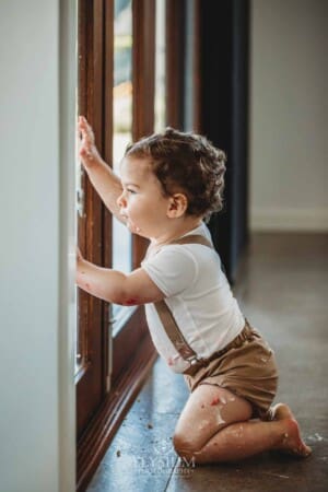 Cake Smash Photographer: a baby boy looks out the window covered in icing