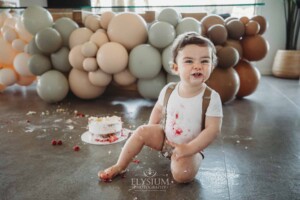 Cake Smash Photographer: a baby boy sits covered in icing pulling faces