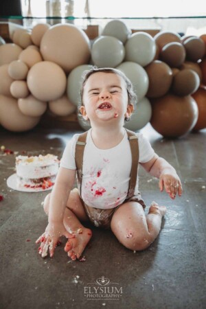 Cake Smash Photographer: a baby boy sits covered in icing pulling faces