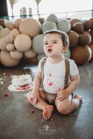 Cake Smash Photographer: a baby boy sits covered in icing pulling faces