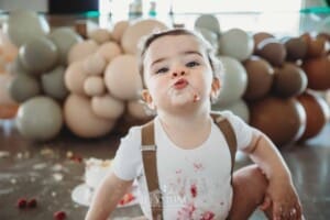 Cake Smash Photographer: a baby boy sits covered in icing pulling faces