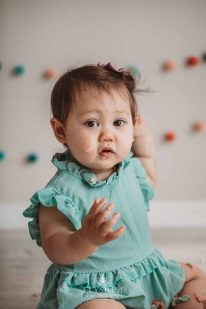 Baby Cake smash Photography: Baby girl wearing a green romper sitting in a bright studio