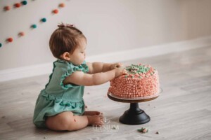 A baby girl plays with her first birthday cake covered in pink and green icing