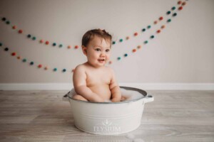 A baby girl sits in a bubble bath tub washing up after her cake smash