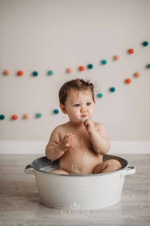 A baby girl sits enjoying a bubble bath in a white vintage tub