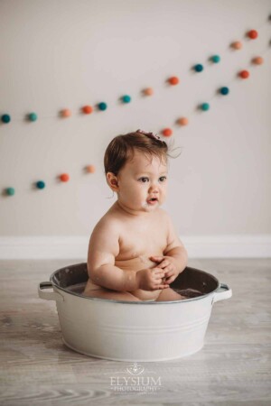 A baby girl sits in a vintage bath tub after her cake smash session