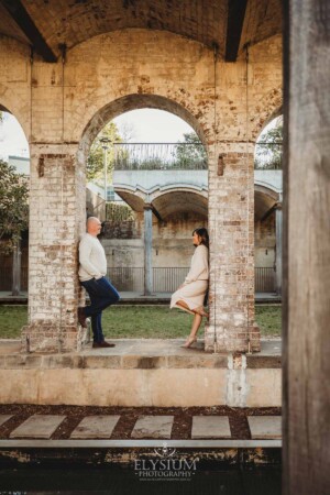 Family Photographer: A couple stand on an old stone wall in Paddington Reservoir Gardens