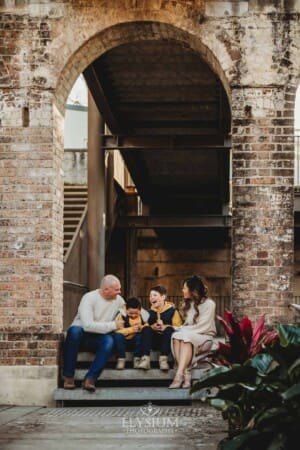 Sydney Family Photographer: parents sit with their sons under a rustic brick arch