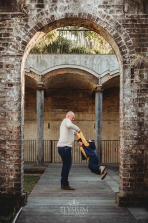 Sydney Family Photographer: dad spins his son around under a rustic brick arch