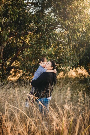 Family Photography: a mother hugs her son in a grassy field at sunset