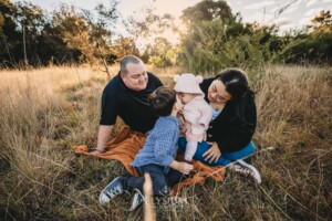 Family Photography: a family sit on a blanket in a grassy field at sunset