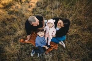 Family Photography: a family sit on a blanket in a grassy field at sunset