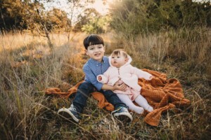 Family Photography: kids sit on a blanket in a grassy field at sunset