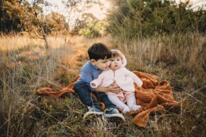 Family Photography: kids sit on a blanket in a grassy field at sunset