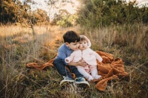 Family Photography: kids sit on a blanket in a grassy field at sunset