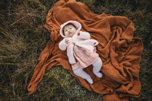 Family Photography: baby girl lays on a blanket in a grassy field at sunset