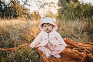 Family Photography: baby girl sits on a blanket in a grassy field at sunset