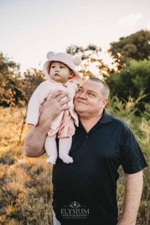 Family Photography: a baby girl sits on her dads shoulders at sunset