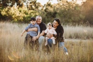 Family Photography: parents sit in a grassy field with their kids