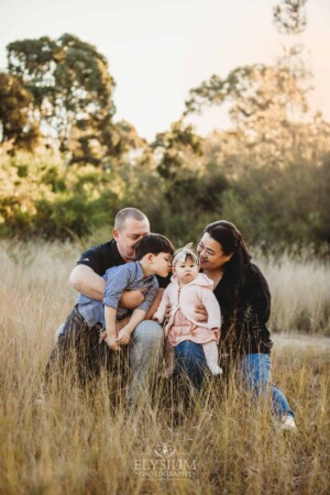 Family Photography: parents sit in a grassy field with their kids
