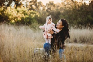 Family Photography: a mother cuddles her baby girl in a grassy field