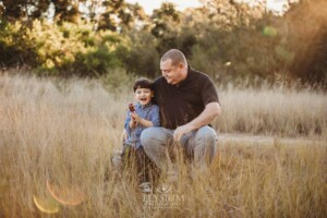 Family Photography: a father hugs his son in a grassy field at sunset