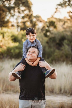 Family Photography: a little boy sits on his dads shoulders at sunset