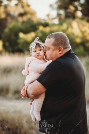 Family Photography: a dad kisses his baby girl in a grassy field