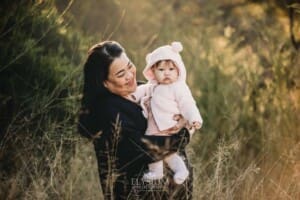 Family Photography: a mother cuddles her baby girl in a grassy field