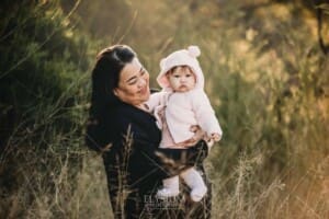 Family Photography: a mother cuddles her baby girl in a grassy field