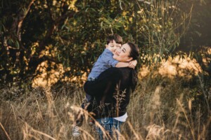 Family Photography: a mother hugs her son in a grassy field at sunset