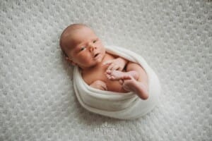 Newborn Photography: a baby boy lays awake on a white textured blanket