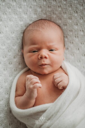 Newborn Photography: a baby boy lays awake on a white textured blanket