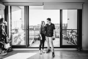 Engagement Photographer: a couple stand cuddling in front of a large bright window