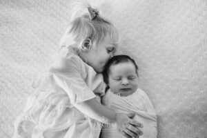 A little girl kisses her baby sister on the head