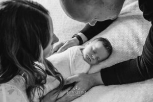 Parents hold their newborn in their hands between them